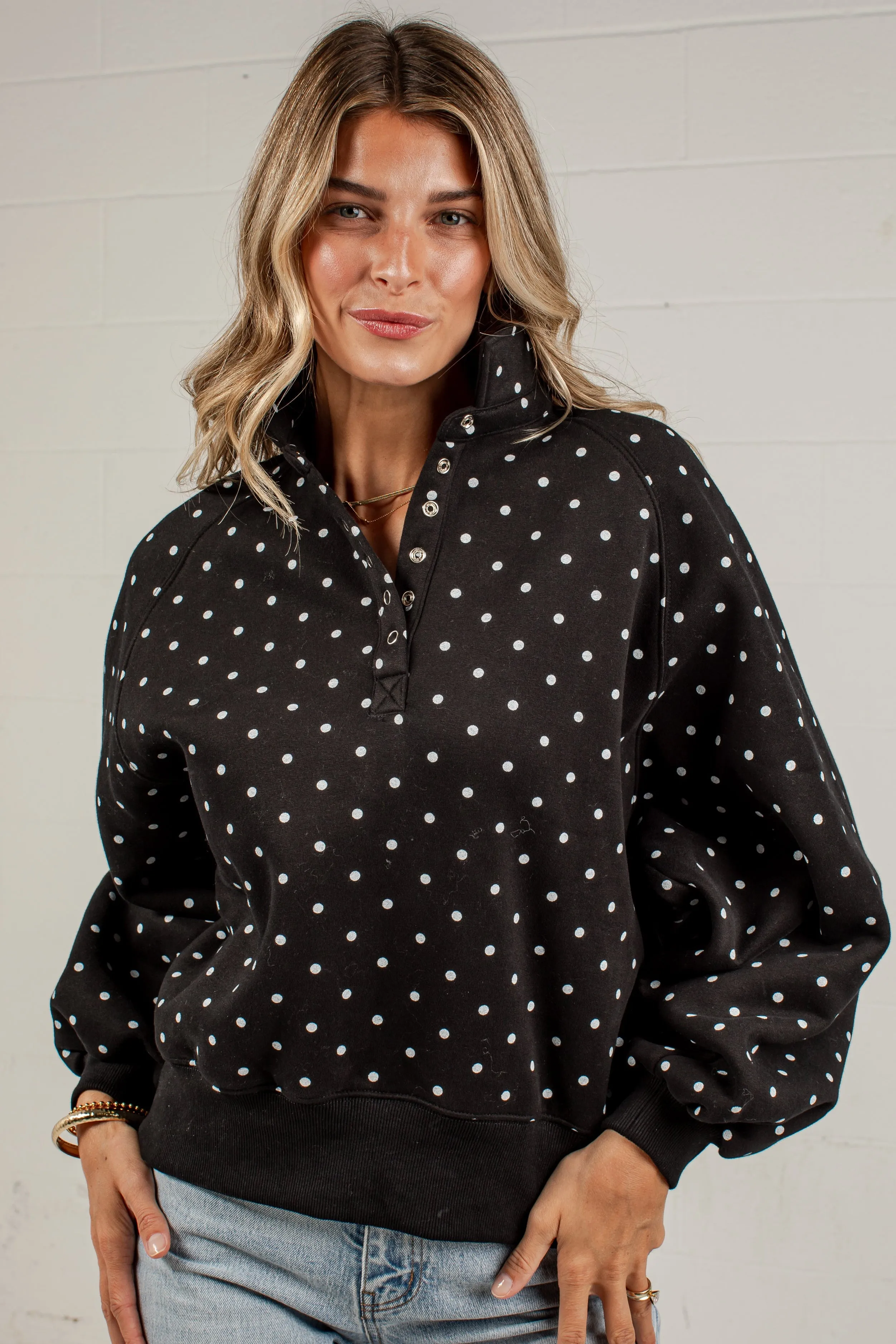 METEORBET88 wanita memakai sweater hitam motif polkadot putih dengan celana jeans